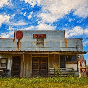 May include: A weathered, light blue building with a flat roof, a front porch, and a wooden door. A vintage red gas pump stands nearby, and a triangular Conoco sign is mounted on a tall wooden post against a bright blue sky with white clouds.