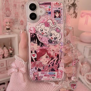 Könnte beinhalten: Eine transparente Handyhülle mit einer Collage aus rosa gehaltenen Anime-Illustrationen, darunter Figuren mit roten und schwarzen Haaren, Herzmotiven und japanischem Text. Die Hülle ist mit einem hängenden Anhänger aus klaren und rosa Perlen versehen.