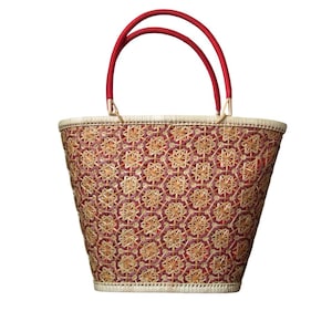 May include: A woven tote bag with a red and tan floral pattern. The bag has red handles and a cream-colored trim. The bag is made of natural materials and is suitable for carrying items.