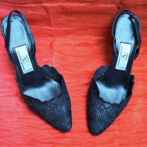 Op de afbeelding: Een paar zwarte pumps met delicate bloemenborduursels. De schoenen hebben een spitse neus en een slingback-band. Het label op de schoenen luidt "Missy Valentino Garavani".
