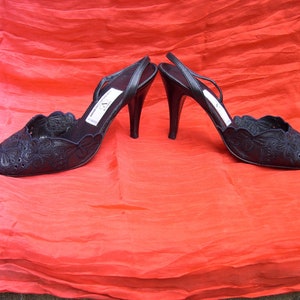 Op de afbeelding: Een paar zwarte pumps met delicate bloemenborduursels. De schoenen hebben een spitse neus en een slingback-bandje.