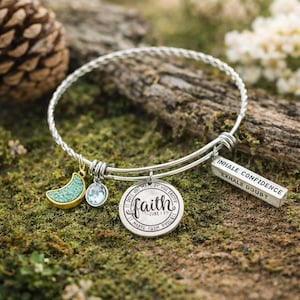 Puede incluir: Una pulsera de alambre trenzado en tono plateado con un dije redondo grabado con la palabra faith y Luke 1:37, un pequeño cristal azul claro, un dije de media luna con borde dorado y un dije rectangular con la inscripción INHALE CONFIDENCE EXHALE DOUBT.