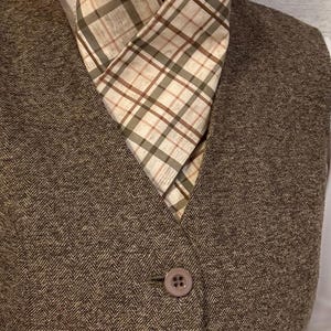 May include: A brown tweed waistcoat with two buttons and a beige and brown plaid cravat.