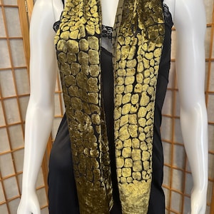 May include: A long scarf featuring a textured, olive green velvet pattern resembling cobblestones or scales set against a sheer black background. The scarf has a rectangular shape with a solid olive green velvet border at the bottom edge.