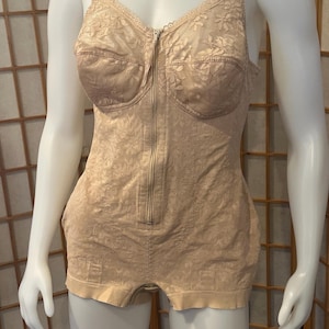May include: A beige, full-body shaper garment featuring a floral lace pattern throughout. This piece includes a front-centre zipper closure, adjustable shoulder straps, and a short-leg design with a finished hemline, providing full torso coverage.