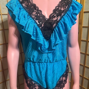 May include: A turquoise romper with black lace trim and a ruffled neckline. The one-piece garment features a V-neck design and short sleeves. The edges of the shorts are also trimmed with black lace.