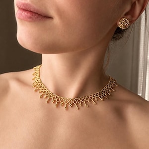 May include: A gold-toned choker necklace featuring a delicate, interconnected lattice pattern with small dangling bead-like accents along the bottom edge, paired with a matching circular stud earring with a textured, honeycomb-like surface.