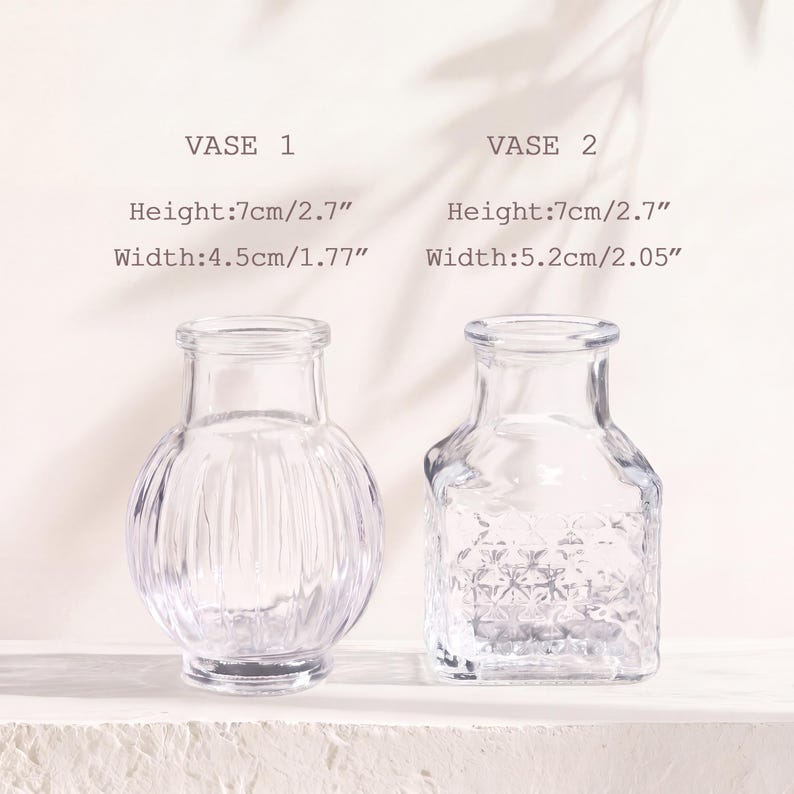 Puede incluir: Dos jarrones de vidrio transparente. El jarr&oacute;n 1 es redondo con estr&iacute;as verticales, 7 cm de alto y 4,5 cm de ancho. El jarr&oacute;n 2 es cuadrado con un patr&oacute;n de diamantes texturizado, 7 cm de alto y 5,2 cm de ancho. Cuellos estrechos y bases anchas.