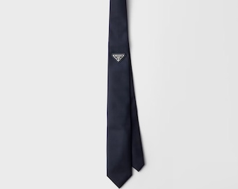 Corbata de lujo de cuero negro de diseñador con placa metálica triangular distintiva y estuche de presentación.