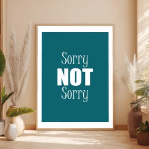 Op de afbeelding: Een ingelijste teal print met de woorden "Sorry NOT Sorry" in witte letters. Het kunstwerk wordt getoond in een kamer met neutrale tinten, met decoratieve planten in vazen en potten.