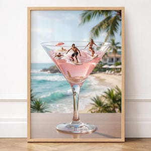 Könnte beinhalten: Gerahmter Druck, der ein großes Cocktailglas zeigt, das mit rosa Flüssigkeit gefüllt ist, mit Miniatur-Surfern, die auf Wellen reiten. Der Hintergrund zeigt eine Strandszene mit Palmen, Meer und sonnigem Himmel. Der Rahmen ist helles Holz.
