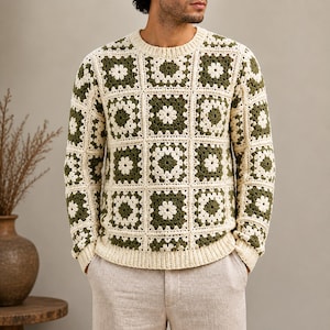 May include: Cream-colored crochet sweater with a floral pattern in olive green. The sweater has a crew neck and long sleeves. The design is made up of square blocks, creating a patchwork effect. The sweater is a medium weight and appears to be handmade.