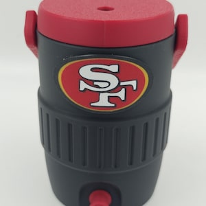 Puede incluir: Enfriador de agua aislado negro y rojo con el logotipo de los 49ers de San Francisco. El enfriador tiene una tapa y un grifo rojos, y un cuerpo negro con un dise&ntilde;o acanalado. Tiene dos asas rojas.