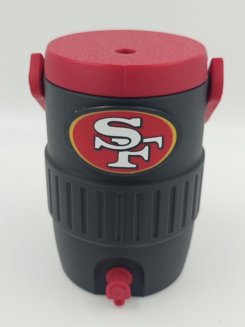 Puede incluir: Enfriador de agua aislado negro y rojo con el logotipo de los 49ers de San Francisco. El enfriador tiene una tapa y un grifo rojos, y un cuerpo negro con un dise&ntilde;o acanalado. Tiene dos asas rojas.