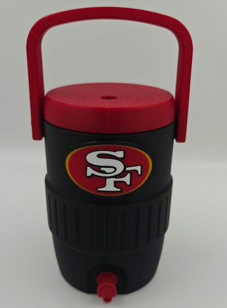 Puede incluir: Enfriador de agua aislado negro y rojo con asa. El enfriador presenta el logotipo de los 49ers de San Francisco en la parte delantera. Tiene una tapa y un asa rojas, y un grifo en la parte inferior para dispensar l&iacute;quidos.