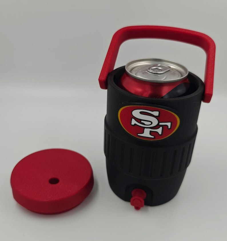 Puede incluir: Enfriador de bebidas aislado negro y rojo con asa y tapa rojas. El enfriador tiene un logotipo de los 49ers de San Francisco y contiene una lata roja. Tiene un peque&ntilde;o grifo rojo en la parte inferior.