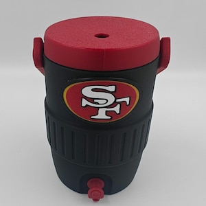 Puede incluir: Enfriador de agua aislado negro y rojo con el logotipo de los 49ers de San Francisco. El enfriador tiene una tapa y asas rojas, un cuerpo negro y un grifo. El logotipo del equipo se muestra en la parte delantera.