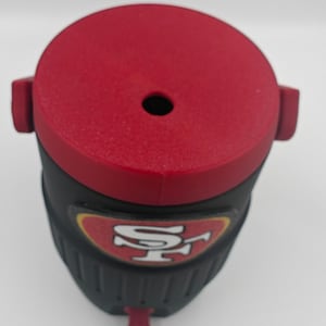 Puede incluir: Un vaso t&eacute;rmico rojo y negro con el logotipo de los 49ers de San Francisco. El vaso tiene una tapa roja con un peque&ntilde;o agujero y una boquilla roja. El cuerpo del vaso es negro con una superficie texturizada.