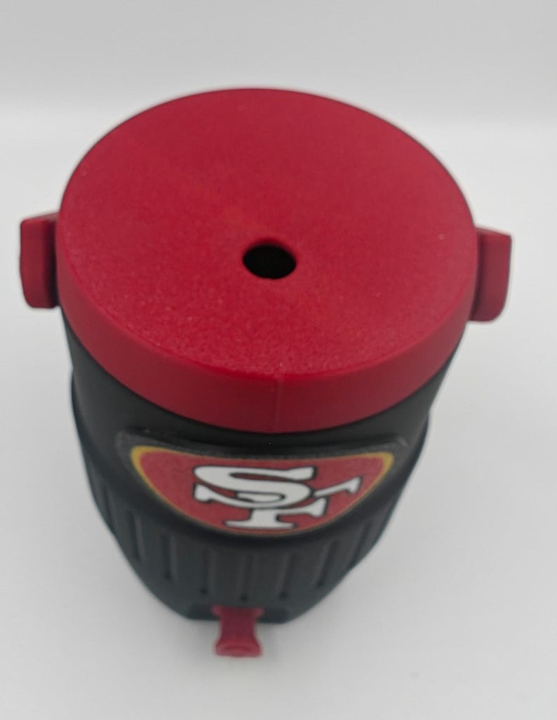 Puede incluir: Un vaso t&eacute;rmico rojo y negro con el logotipo de los 49ers de San Francisco. El vaso tiene una tapa roja con un peque&ntilde;o agujero y una boquilla roja. El cuerpo del vaso es negro con una superficie texturizada.