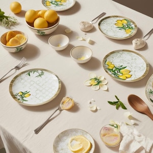 Puede incluir: Una mesa decorada con platos decorativos, cuencos y utensilios para servir. Los platos y cuencos tienen un fondo blanco con un diseño de limón verde y amarillo. Hay limones frescos en un cuenco y rodajas de limón en un cuenco pequeño.