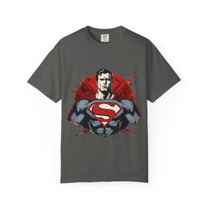 May include: Dark grey t-shirt with a Superman graphic. The design features Superman's chest with the iconic "S" symbol, a red cape, and a red circle backdrop. The t-shirt has a classic crew neck.