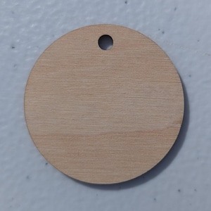 May include: A round, unfinished wooden tag with a small hole at the top for hanging. The tag is made of light-colored wood and has a visible wood grain pattern. The tag is approximately 2 inches in diameter.