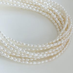 Peut inclure: Un collier multi-rangs composé de nombreuses petites perles d'eau douce blanches de forme ovale. Les perles sont enfilées en plusieurs rangées parallèles, créant un agencement incurvé et superposé avec une finition de surface lustrée.