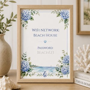 Puede incluir: Un marco de madera clara que contiene un letrero con detalles florales de hortensias azules, una ilustración de paisaje costero y el texto: WIFI NETWORK: BEACH HOUSE, PASSWORD: BEACH123. El letrero presenta un pequeño icono de concha marina.
