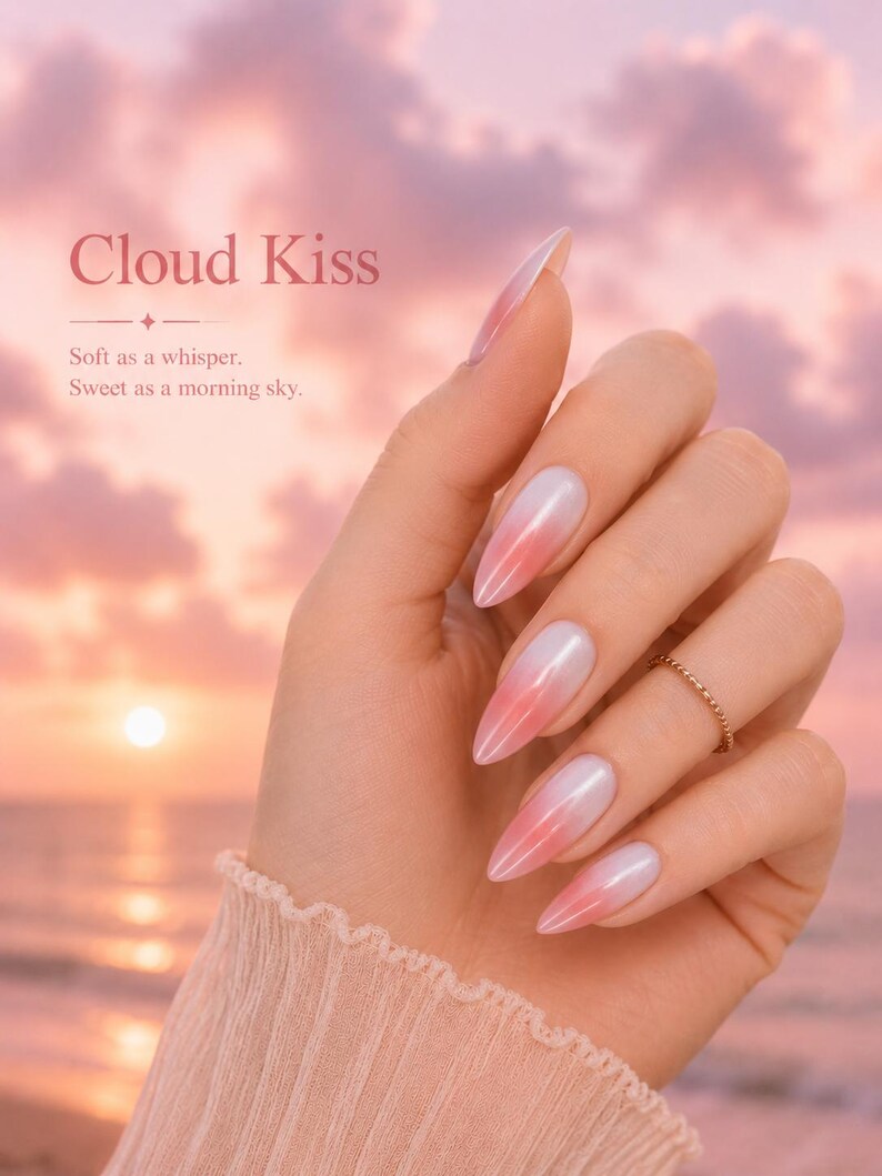 May include: A hand with long, almond-shaped nails painted with a gradient of white to pink. The nails are the focal point, with a gold ring on the ring finger. The background is a soft, pink sunset with the text "Cloud Kiss".