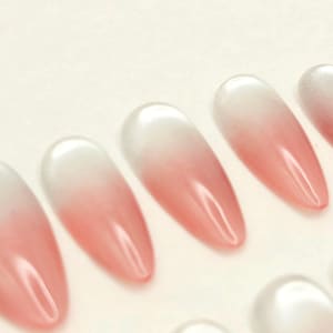 May include: A collection of almond-shaped artificial nails. Each nail features a gradient design, transitioning from a white base to a soft pink hue. The nails have a glossy finish, reflecting light.