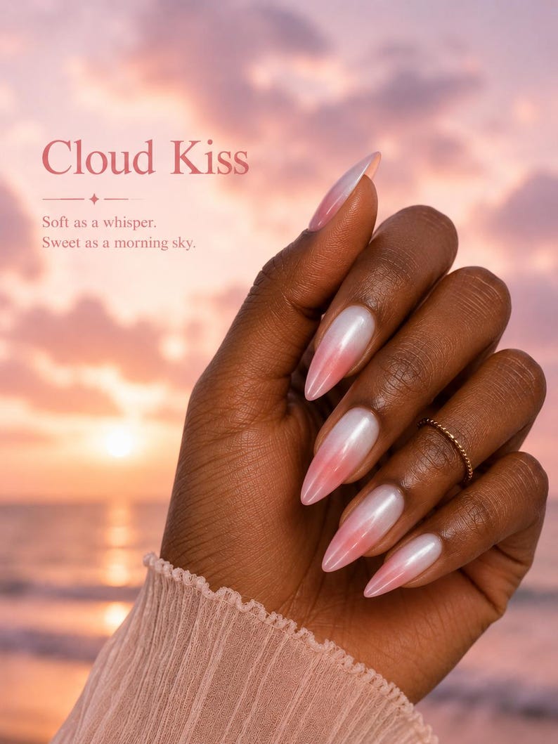 May include: A hand with long, almond-shaped nails featuring a gradient design, transitioning from a pearlescent white at the base to a soft pink at the tips. The nails are set against a sunset backdrop, with the text "Cloud Kiss".