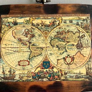 May include: A rectangular wooden wall plaque featuring a vintage-style world map print with the word PEACE overlaid in large gold letters. The plaque has a dark, scorched-look border and includes a small metal hanging loop at the top center.