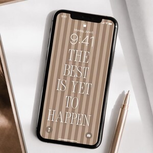 Può includere: Uno smartphone con cornice nera mostra l'ora 9:41 e il testo "THE BEST IS YET TO HAPPEN" su uno sfondo a righe. Una penna dorata è appoggiata su un taccuino bianco.