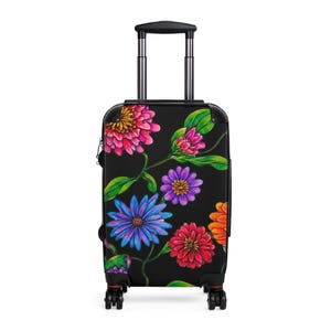 Könnte beinhalten: Ein schwarzer Rollkoffer mit einem lebendigen Blumenmuster in Pink, Lila, Blau, Rot und Orange sowie grünen Blättern. Das Gepäckstück verfügt über einen ausziehbaren silbernen Griff, schwarze Eckschoner und vier schwarze Rollen.