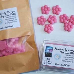 Puede incluir: Derretidos de cera de soja rosas en forma de flor, algunos sueltos y otros en un recipiente de plástico transparente y una bolsa de papel marrón. El embalaje incluye etiquetas con el texto: "Kreations by Kerry 55 Soy Wax Melts" y "Scent - Spa Retreat."