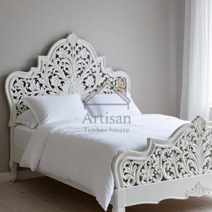 Peut inclure: Un lit en bois blanc sculpté avec un motif floral. La tête de lit et le pied de lit présentent des sculptures détaillées. Le lit est fait avec une literie et des oreillers blancs. Le logo Artisan Timber House est visible.