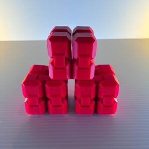 May include: A bright red, geometric puzzle toy composed of interlocking, articulated blocks. The blocks are arranged in a symmetrical pattern, showcasing the toy's modular design. The vibrant color and angular shapes create a visually engaging product.