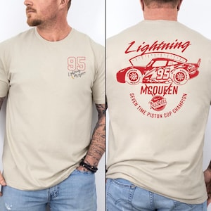 Puede incluir: Una camiseta beige con un pequeño logotipo rojo 95 en el pecho. La parte posterior muestra un gran gráfico rojo de un coche de carreras con el texto Lightning McQueen, Seven Time Piston Cup Champion y un logotipo de Rust-eze en diseño circular.