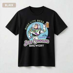 May include: A black short-sleeve t-shirt featuring a graphic of a space ranger character holding a beer mug. The text reads BUZZ LITE BEER, BEST QUALITY SINCE 1995, STAR COMMAND BREWERY. The design is set against a light blue circular background.
