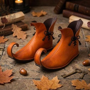 May include: A pair of tan leather ankle boots featuring a distinctively curved, pointed toe design. The boots have a dark brown interior lining and are secured with thin black laces tied in small bows at the outer sides of the ankle openings.