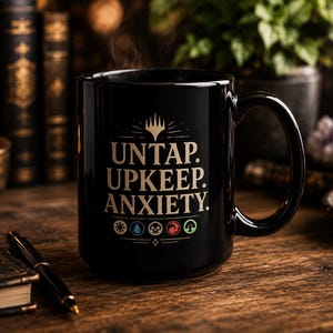 May include: Black ceramic mug with the text "UNTAP. UPKEEP. ANXIETY." in white. The mug features a large handle and symbols at the bottom. Steam rises from the mug, suggesting a hot beverage. The mug is on a wooden surface.