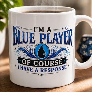 May include: White ceramic mug with the text "I'M A BLUE PLAYER OF COURSE I HAVE A RESPONSE" in blue. The mug features a blue and black graphic design and is filled with a dark liquid, possibly coffee.