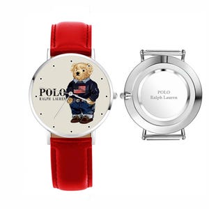 May include: A red leather strap watch with a cream-colored face featuring a bear wearing a navy blue sweater and jeans. The watch face has the text "POLO Ralph Lauren". The watch's back is silver with the text "POLO Ralph Lauren".