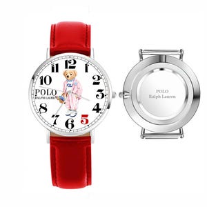 May include: A Polo Ralph Lauren wristwatch with a red leather strap and a white face featuring a bear illustration, black numerals, and the text Polo Ralph Lauren. Beside it is a separate silver-tone watch case back with the same brand text.