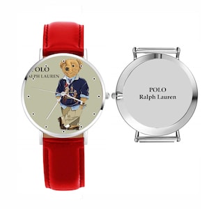 May include: A wristwatch with a red leather band and a silver-tone case. The watch face features a cartoon bear wearing a navy blue sweater and khaki pants. The watch face also has the text "POLO Ralph Lauren".