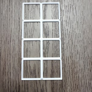 May include: A white plastic grid with eight evenly spaced square openings. The grid is rectangular and appears to be made of thin, connected bars. The background is a wooden surface.