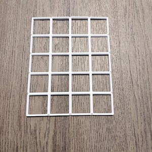 May include: A white plastic grid with a rectangular shape, composed of evenly spaced squares. The grid is positioned on a wooden surface with a natural wood grain pattern.