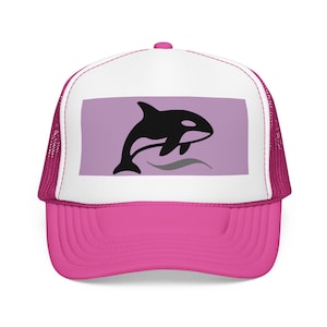 May include: A pink trucker hat. The white front panel displays a black orca whale leaping over grey waves on a lavender background. The hat has a pink brim and a pink mesh back.