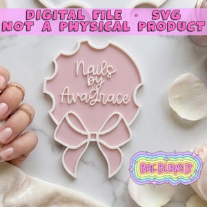 May include: A light pink circular sign with a white border and a white bow at the bottom. The text 'Nails by Avagrace' is written in white script in the center. The sign is a digital file SVG. A small logo with the text 'BRE BURNS IT' is visible.