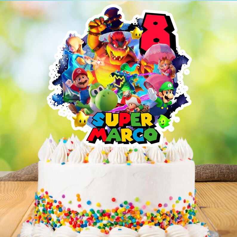 May include: A white frosted cake with colorful sprinkles and a Super Mario themed topper. The topper features various characters, the number 8, and the name "SUPER MARCO" in bold, colorful letters.